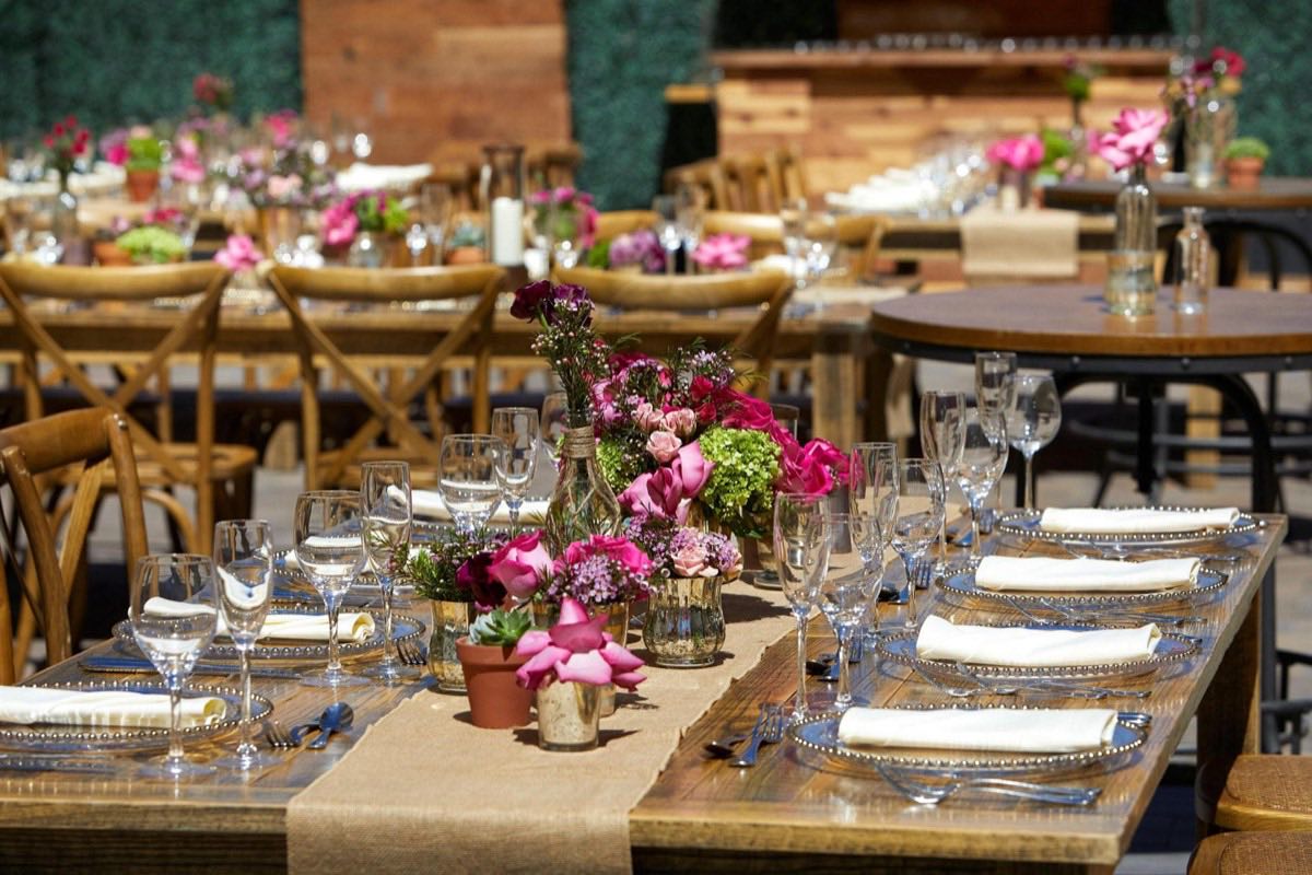 Outdoor event tables dressed with pink florals and rustic wood chairs
